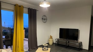 Uma sala de estar moderna com uma TV grande, uma mesa pequena e um vaso decorativo.