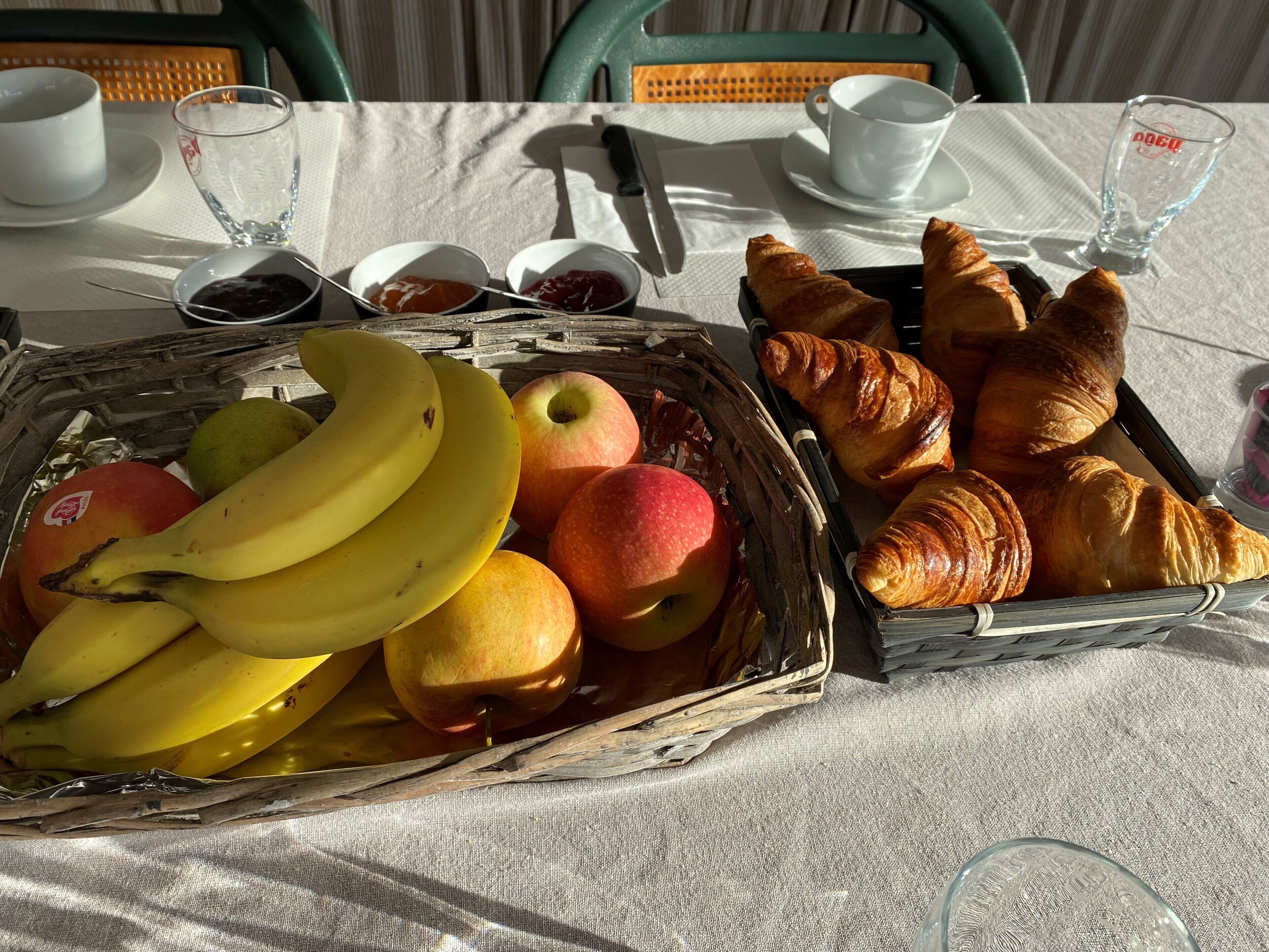 A table with a basket of fruits and pastries, a cup, and a napkin.