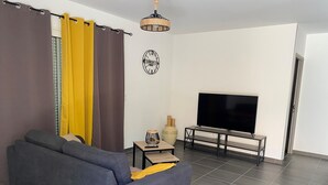 Sala de estar com sofá cinza, televisão em móvel, abajur decorativo e relógio de parede.