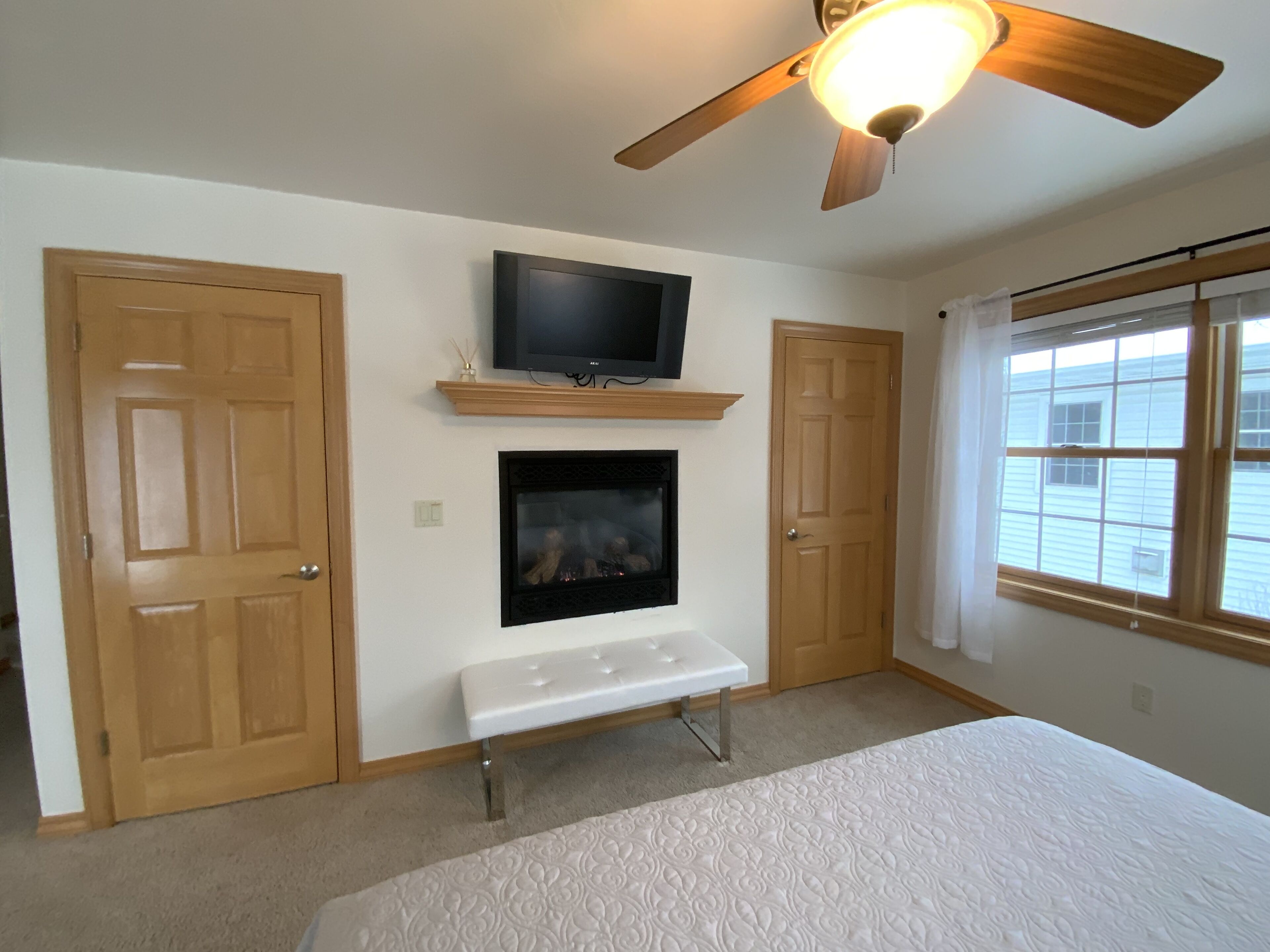 A bedroom with a bed, a television, a fireplace, and a ceiling fan.