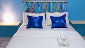 A bed with white bedding, two blue pillows, and a neatly folded white towel. - Oxe Rooms (Salvador)
