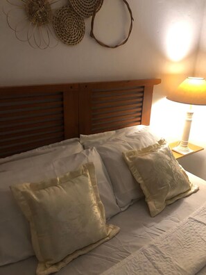 A bed with white bedding and two pillows, a wooden headboard, and a wall with woven wall hangings. - Oxe Rooms (Salvador)
