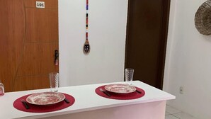 A small, modern kitchen with a white countertop, two black bar stools, and a wooden door marked with the number 101. - Oxe Rooms (Salvador)