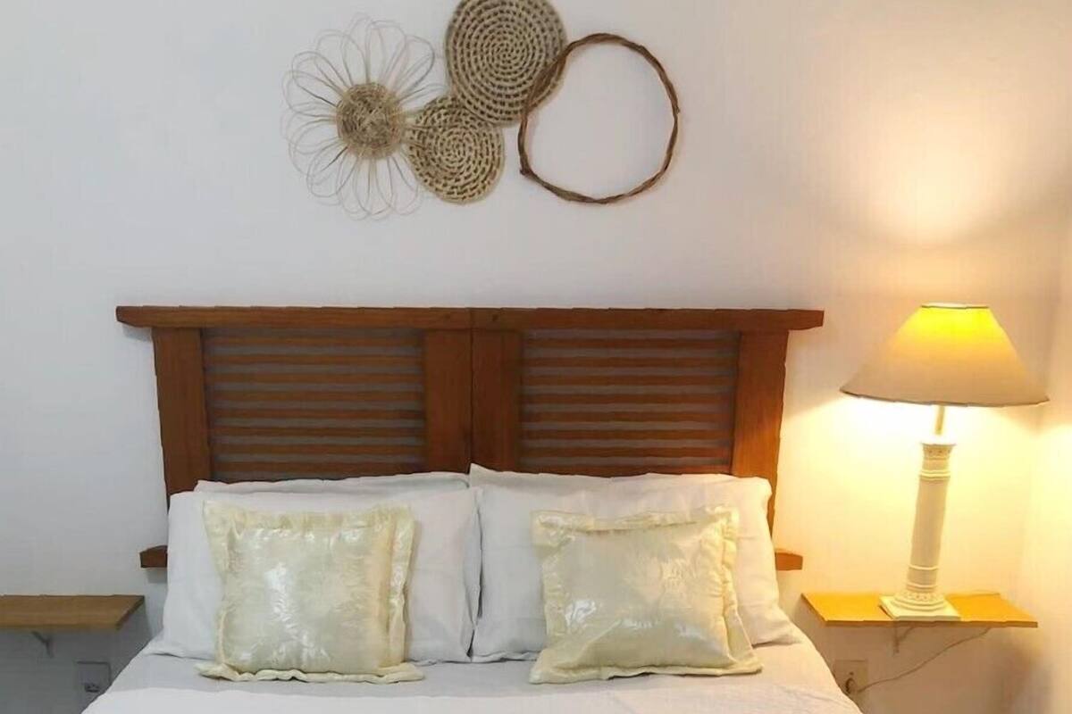 A neatly made bed with white linens and rolled towels, a wooden headboard, a bedside lamp, and decorative wall art.
