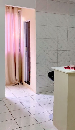 A room with a tiled floor, a white wall with a marble pattern, a doorway with a curtain, and a small table with a red object on it. - Oxe Rooms (Salvador)
