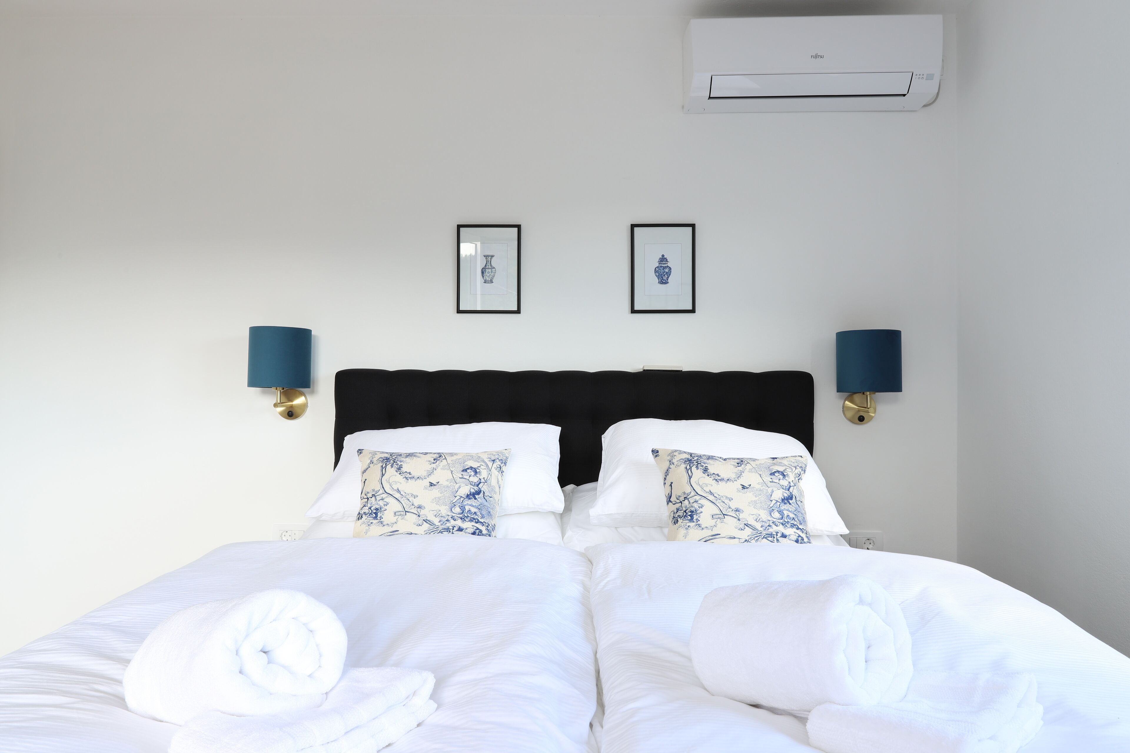 Ett hotellrum med en säng, två väggmonterade luftkonditioneringsapparater och två inramade tavlor.