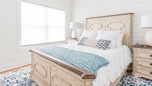 Un dormitorio con cama de madera, ropa de cama blanca, una ventana y una mesita de noche con lámpara.