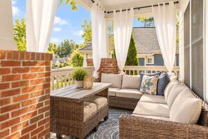 A covered outdoor seating area with wicker furniture, a small table, and a potted plant.