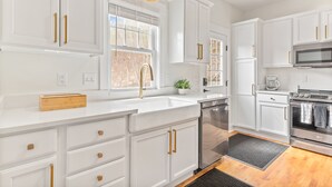Una cocina moderna con armarios blancos, tiradores dorados, lavavajillas de acero inoxidable y horno integrado.