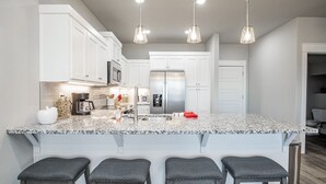 A modern kitchen with white cabinets, a stainless steel refrigerator, a granite countertop, and four bar stools. - Close to everything, New Fayetteville Home! (Fayetteville)