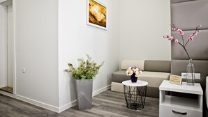 Un moderno vestíbulo de hotel con un sofá gris, una mesita redonda con un jarrón de flores, una planta en maceta y un cuadro abstracto enmarcado en la pared.
