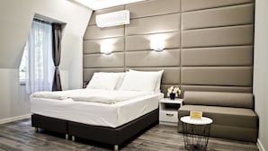 Un dormitorio moderno con una cama grande, cabecera con iluminación integrada, una mesita de noche con una lámpara pequeña y una ventana con cortinas.