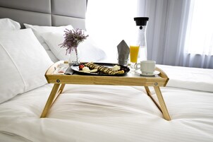 A neatly made bed with white linens, a tray with breakfast items, a vase with flowers, and a bottle of orange juice.