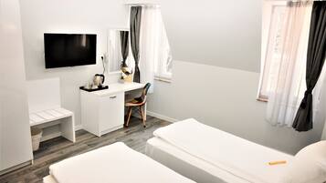 A hotel room with a bed, a desk, a chair, a TV, and a window with curtains.