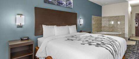 Quarto de hotel com uma cama grande, uma mesa de cabeceira, uma luminária na parede, um quadro e um banheiro com banheira.