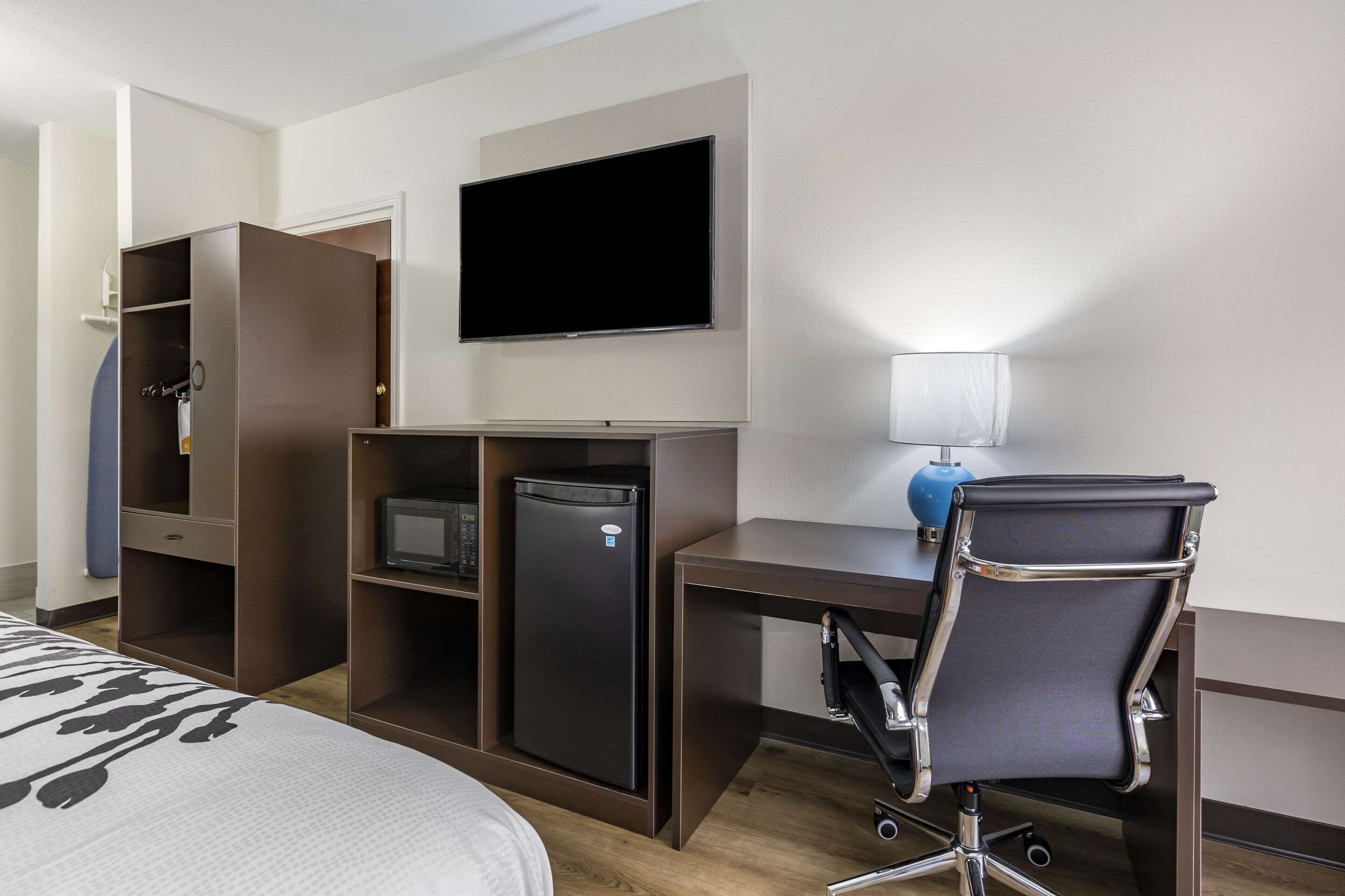 Une chambre d’hôtel comprenant un lit, un bureau avec une chaise, une télévision, un mini-réfrigérateur et une armoire.