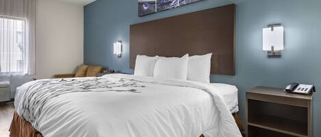 A hotel room with a large bed, a bedside table with a phone, a wall-mounted light, and a painting above the bed.