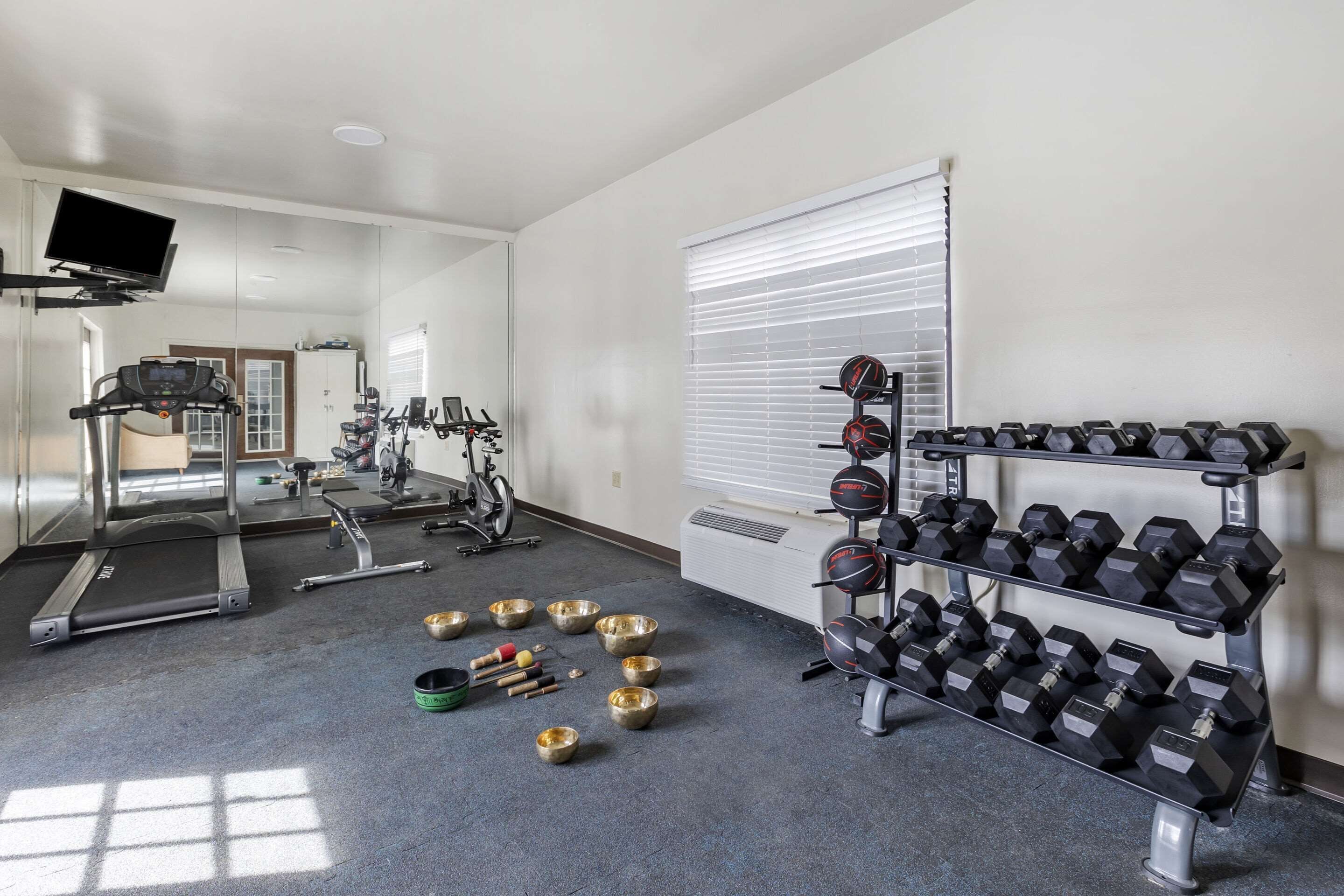 A gym with exercise equipment, a treadmill, dumbbells, and a TV mounted on the wall.