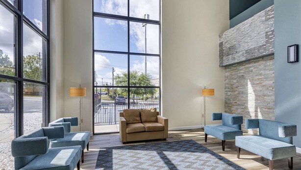 Eine moderne Lobby mit großen Fenstern, einer Wand aus Stein und verschiedenen Sitzgelegenheiten, darunter Sofas und eine Zweiseitercouch.