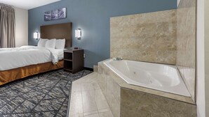 Ein Hotelzimmer mit Bett, Nachttisch, Wandlampe, großem Spiegel und Badewanne.