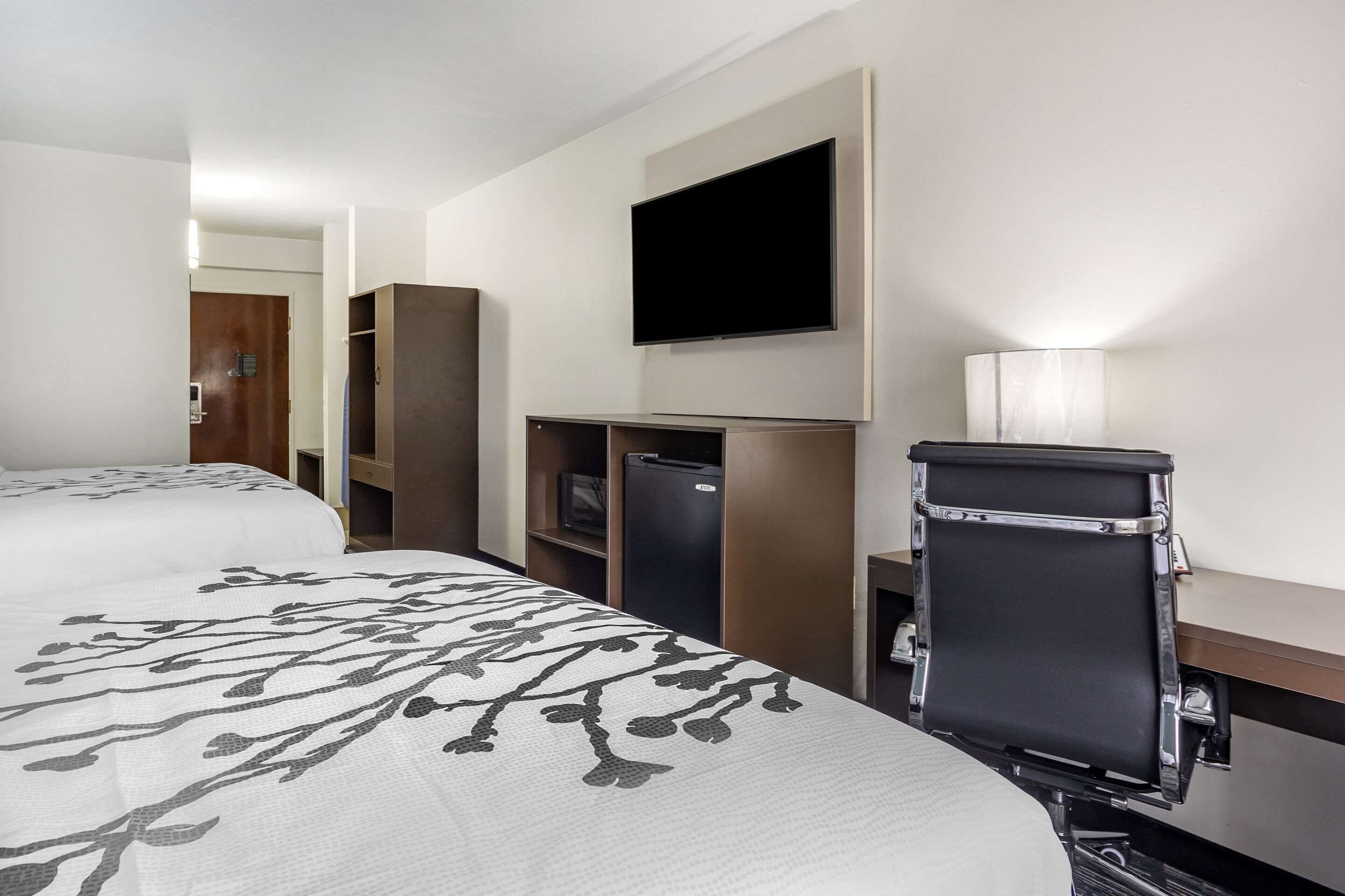 Una habitación de hotel con cama, escritorio, televisor, lámpara y armario.