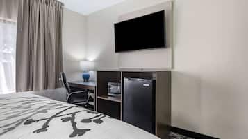 Een hotelkamer met een bed, een bureau met een computer, een televisie en een minibar.