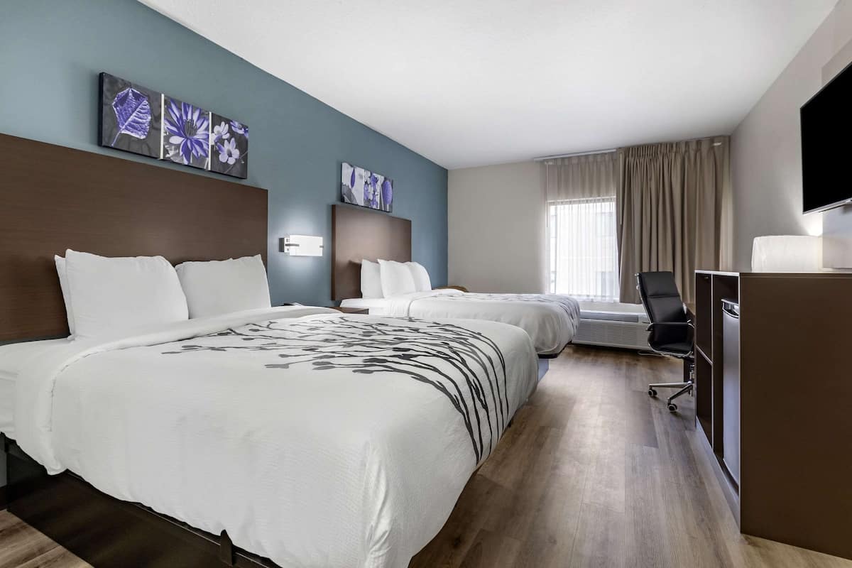 Ett hotellrum med två sängar, ett skrivbord, en stol och konstverk på väggarna.