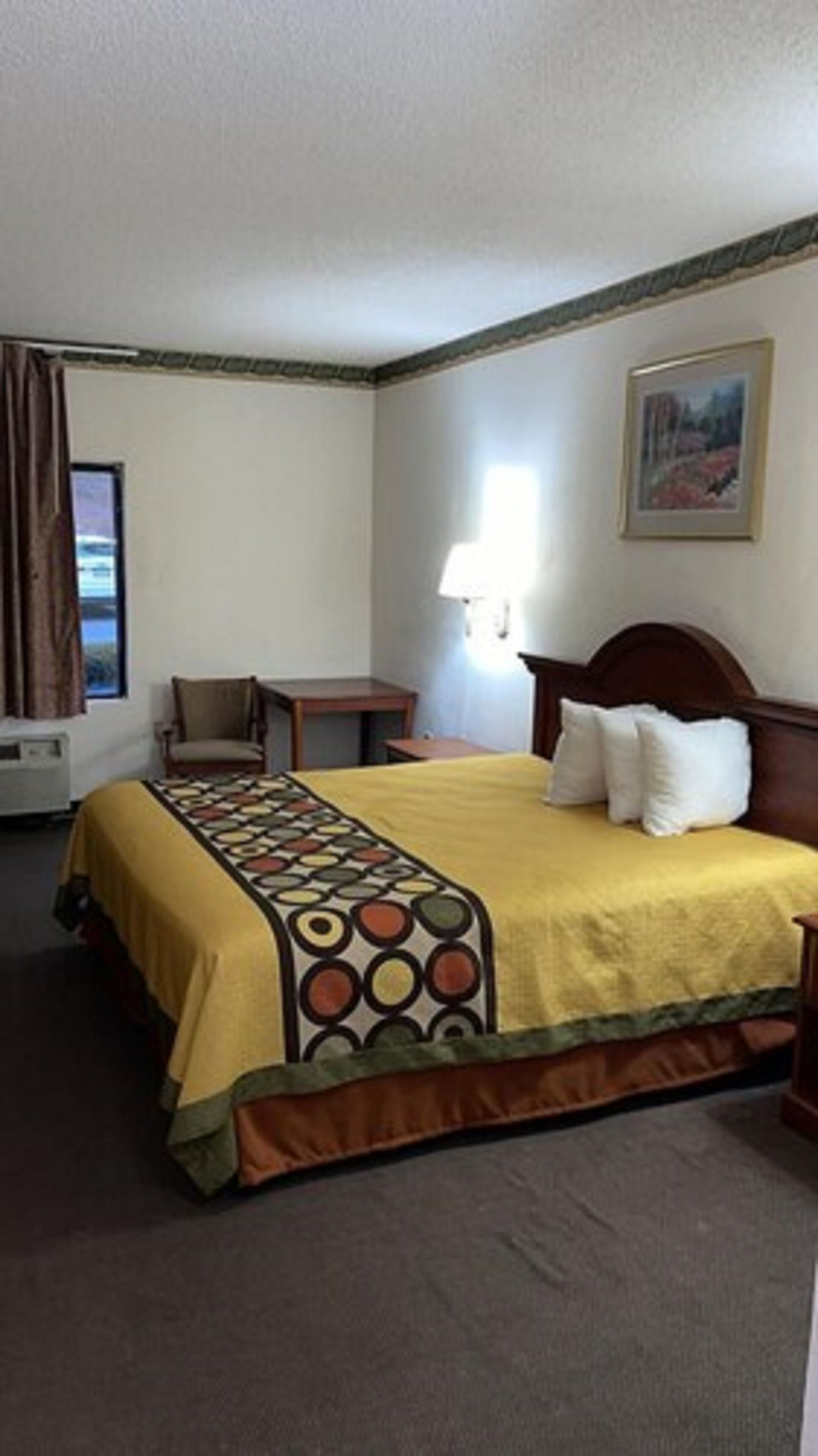 A hotel room with a bed, a chair, a small table, and a window with curtains.