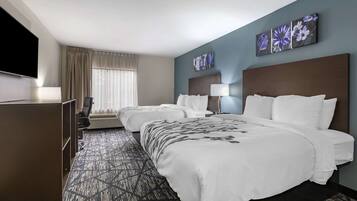 Quarto de hotel com uma cama grande, uma cama menor, uma escrivaninha e uma televisão.