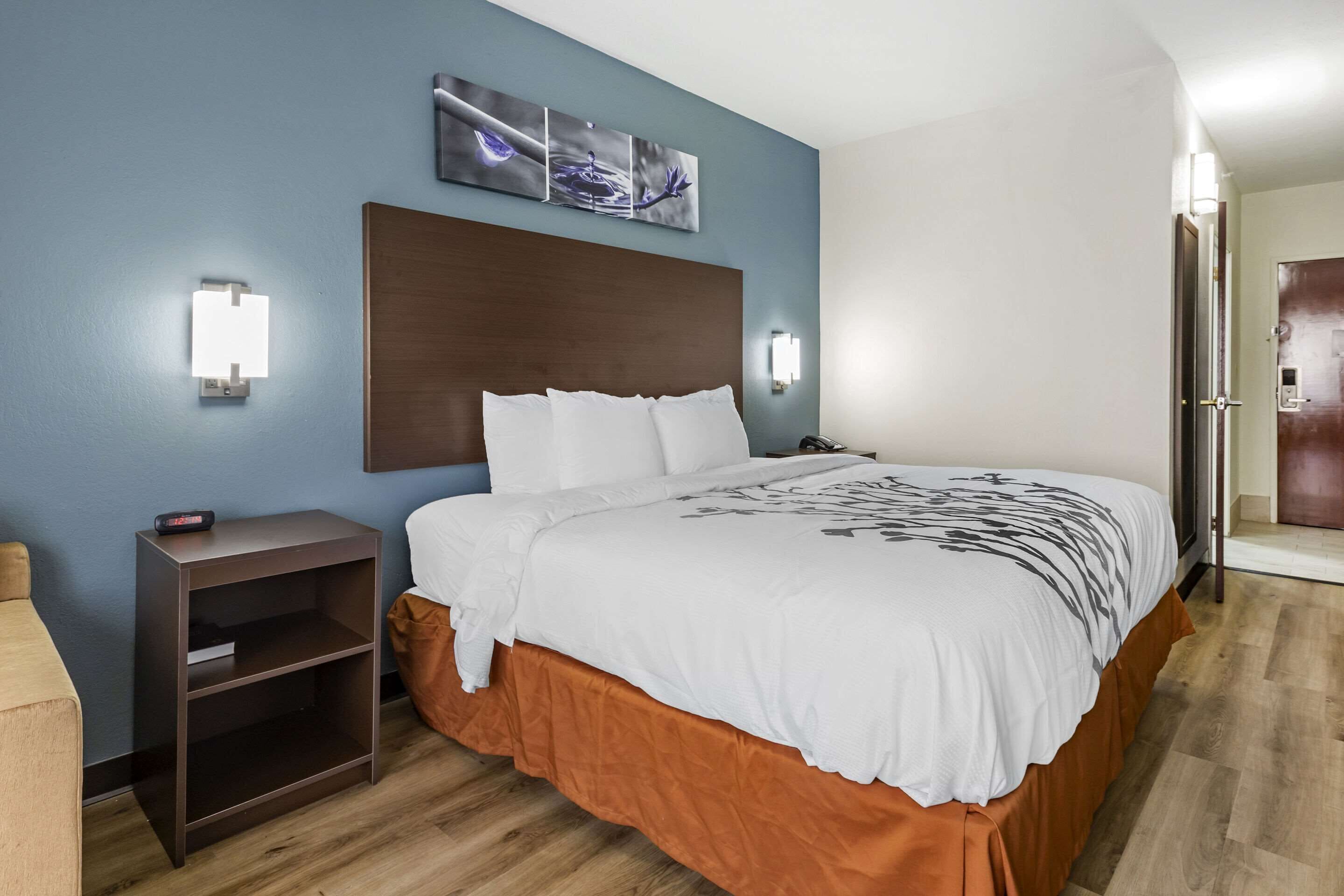 A hotel room with a large bed, a nightstand, a wall-mounted light, and a door.