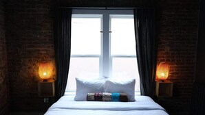 Ein Hotelzimmer mit einem großen Bett, zwei Nachttischlampen, einem mit Vorhängen versehenen Fenster und Ziegelwänden.