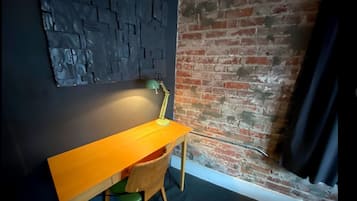 Habitación de esquina con un escritorio de madera, una silla verde, una lámpara y una pared de ladrillo.