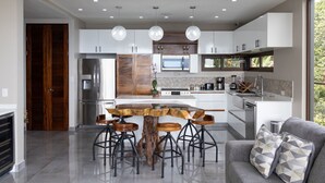 Una cocina moderna con una isla central, taburetes de bar, una mesa de madera y un horno empotrado.