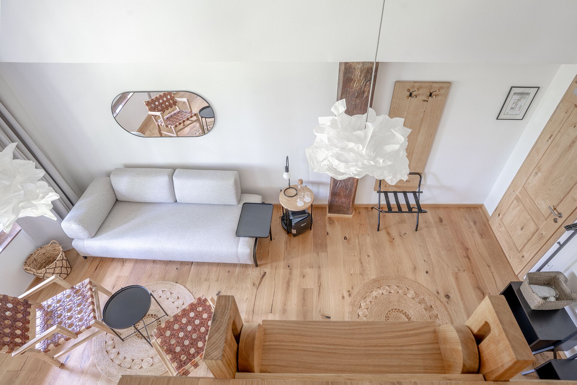 A compact living space with a sofa, a small round table, a chair, a hanging light fixture, and a wooden cabinet.