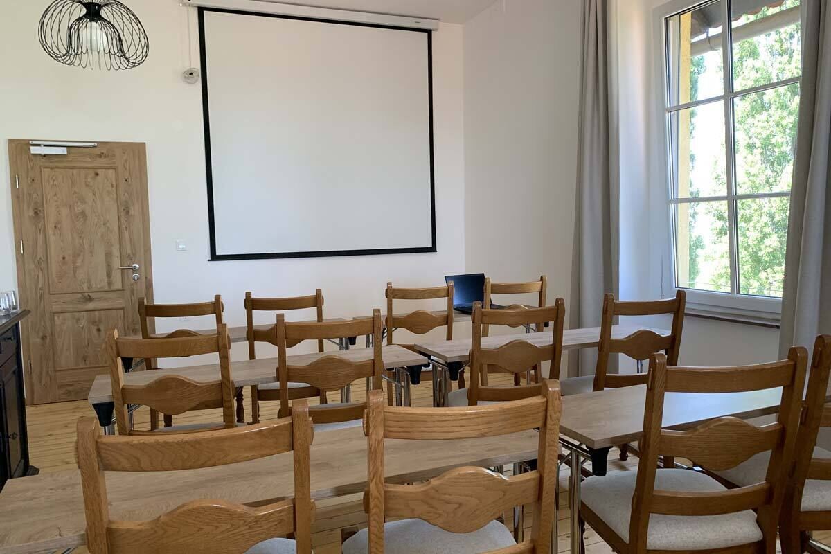 A conference room with wooden tables and chairs, a projector screen, and a window with curtains.