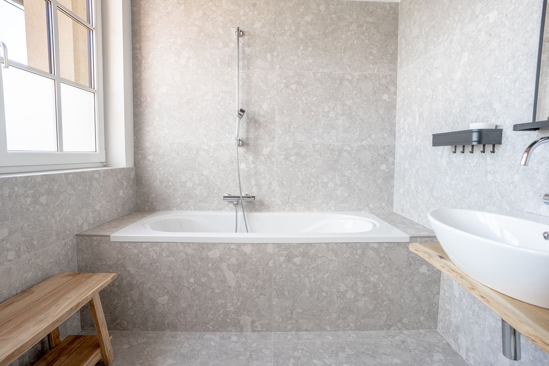 Un baño moderno con una bañera independiente, un banco de madera y un espejo grande.