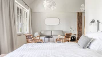 Et soveværelse med en stor seng, to fletstole, et lille rundt bord, en sofa og en vægmonteret lampe.