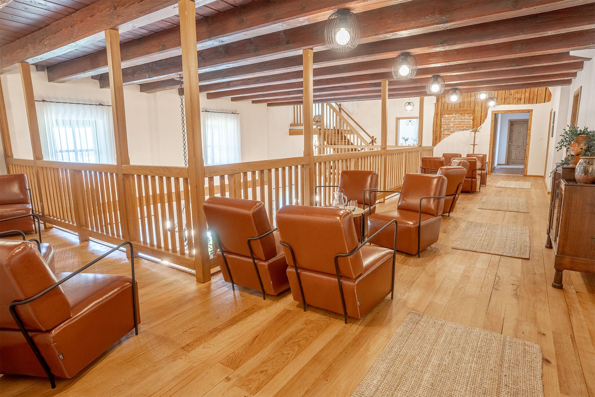 A spacious room with wooden floors, a wooden railing, and leather chairs arranged for seating.