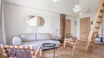 Una sala de estar moderna con un sofá, dos sillas, una mesita, un espejo y una escalera de madera.
