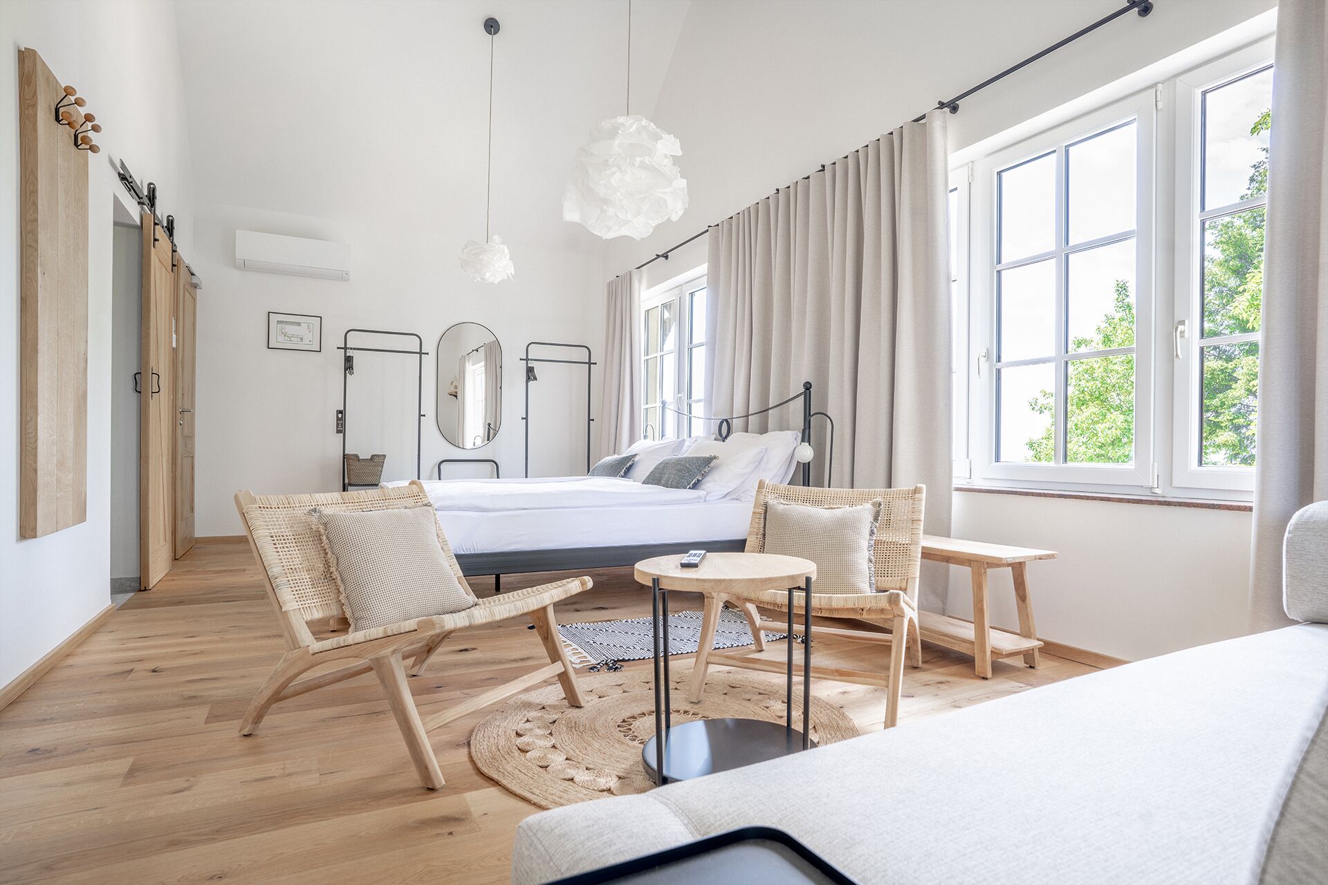 Une chambre moderne avec un lit, deux chaises, une petite table et une grande fenêtre.