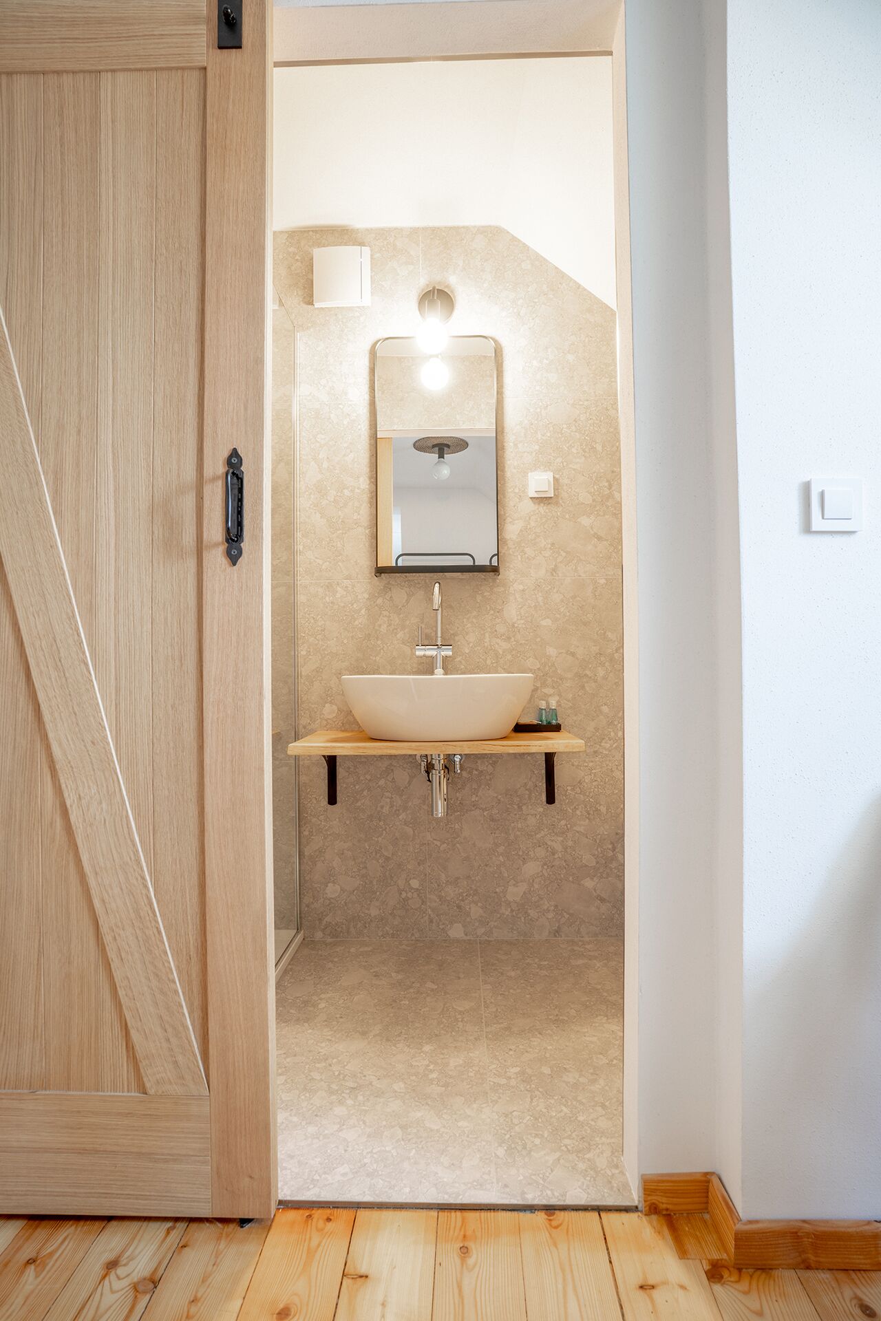 Un baño moderno con puerta de madera, un lavamanos independiente y un espejo sobre él.