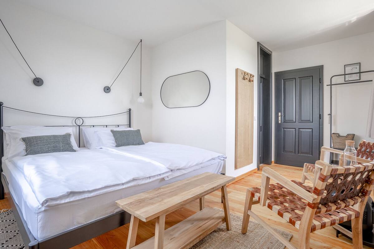 Un dormitorio con cama, mesitas de noche, un banco de madera y una silla.