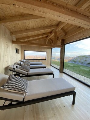 Un intérieur en bois avec quatre chaises longues et une grande fenêtre donnant sur un paysage.