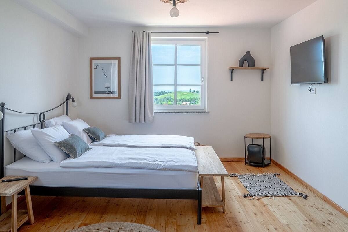 Un dormitorio con cama, ventana, televisor y una mesita.