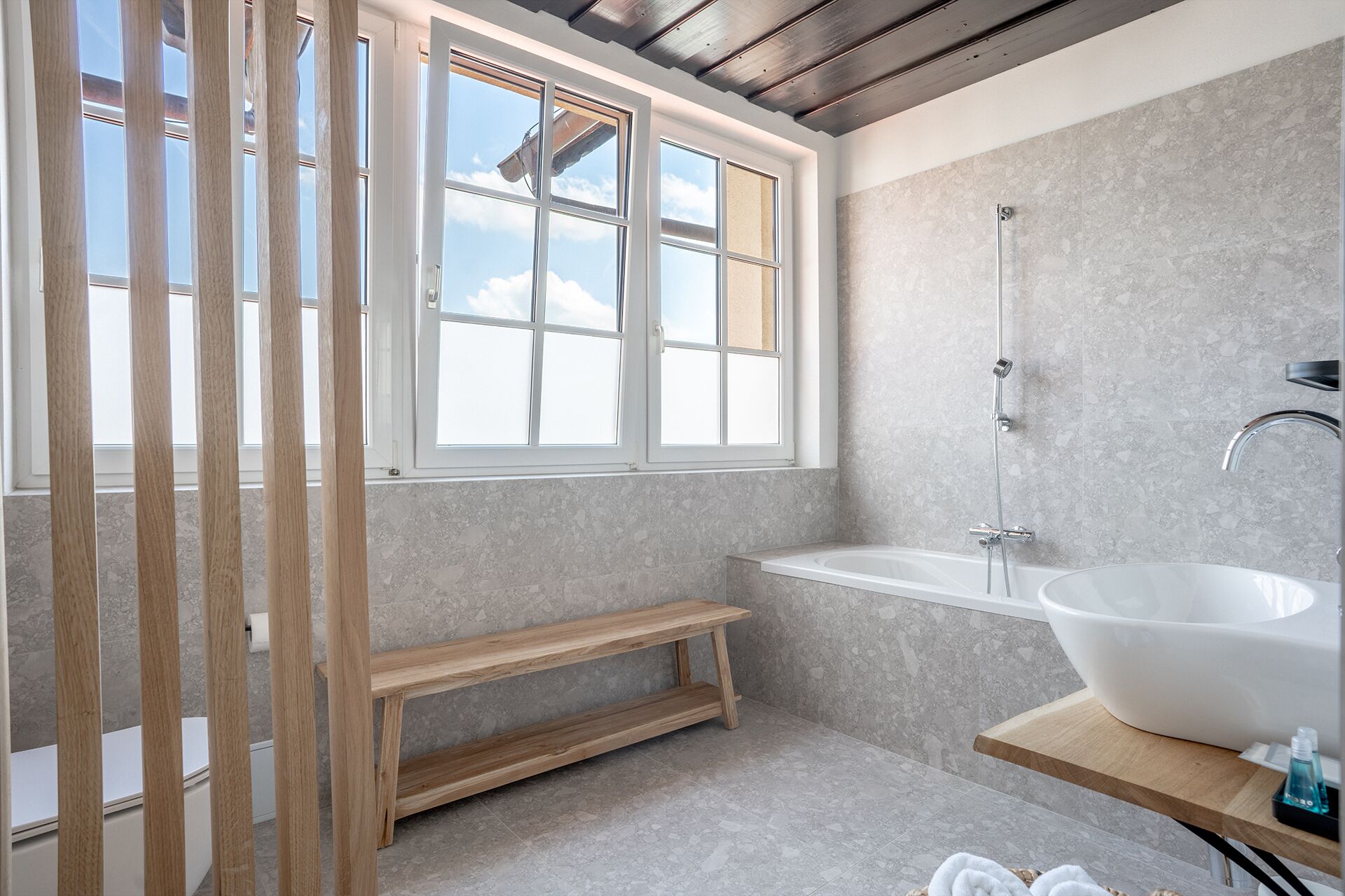 Une salle de bain moderne dotée d’une grande fenêtre, d’une baignoire sur pieds et d’un banc en bois.