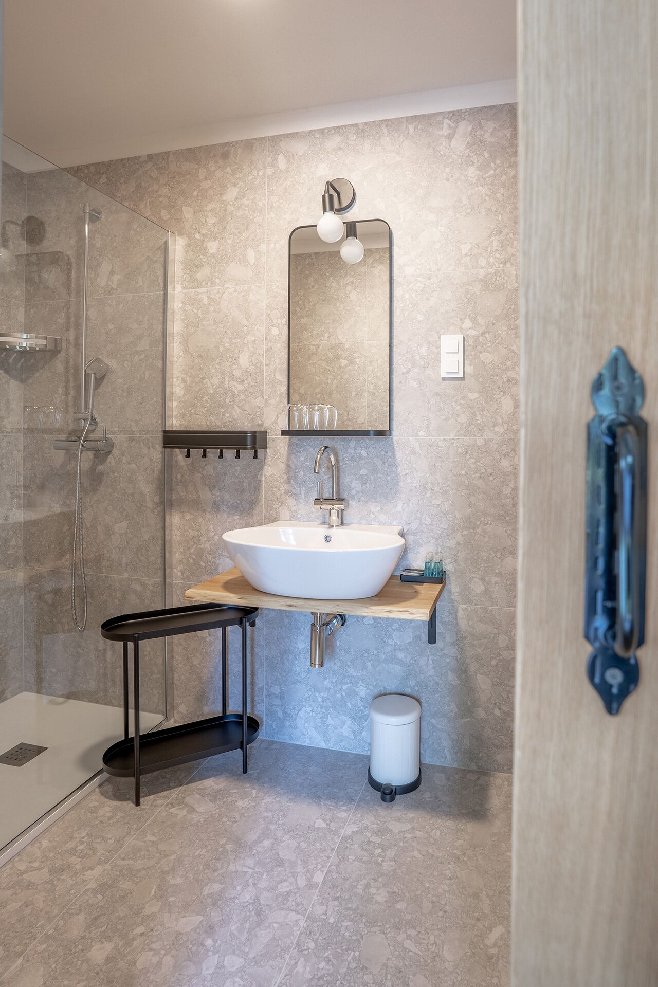 A modern bathroom with a freestanding sink, a glass shower enclosure, and a mirror with a round light fixture.