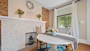 Un comedor con chimenea de ladrillo, una mesa con sillas y vistas a través de una ventana.