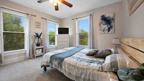 Un dormitorio con una cama, ventilador de techo, televisor y ventanas amplias.