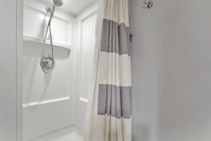 A bathroom with a shower, a curtain, and a wall-mounted light fixture.