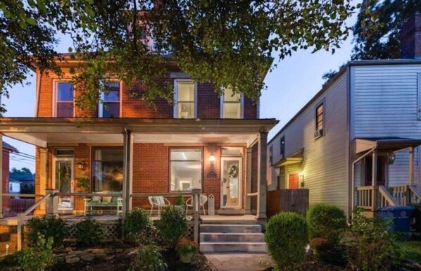 A two-story house with a covered porch, a brick facade, and a small front yard.